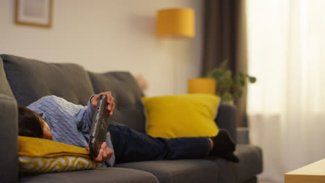 Young-Boy-Lying-On-Sofa-At-Home-Playing-Game-Or-Streaming-Onto-Handheld-Gaming-Device-9